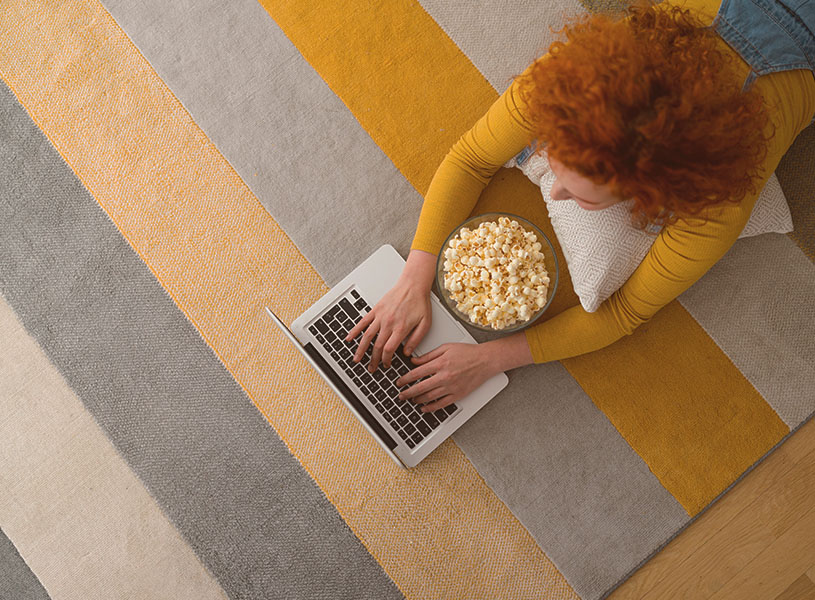 大胆なストライプ柄のラグに寝転んでパソコンを打つ女性